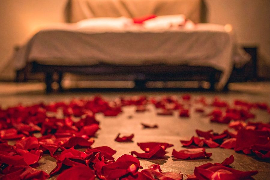 A floor covered in red rose petals with a blurred bed in the background