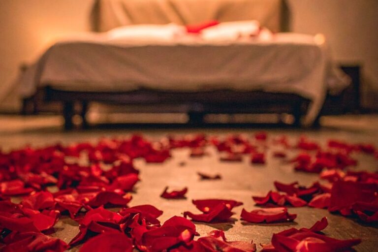 A floor covered in red rose petals with a blurred bed in the background