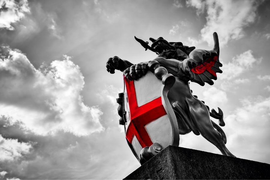 Statue of St George slaying the dragon with red cross shield against dramatic sky